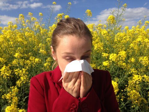 Woman blowing her nose with yellow flowers in the background