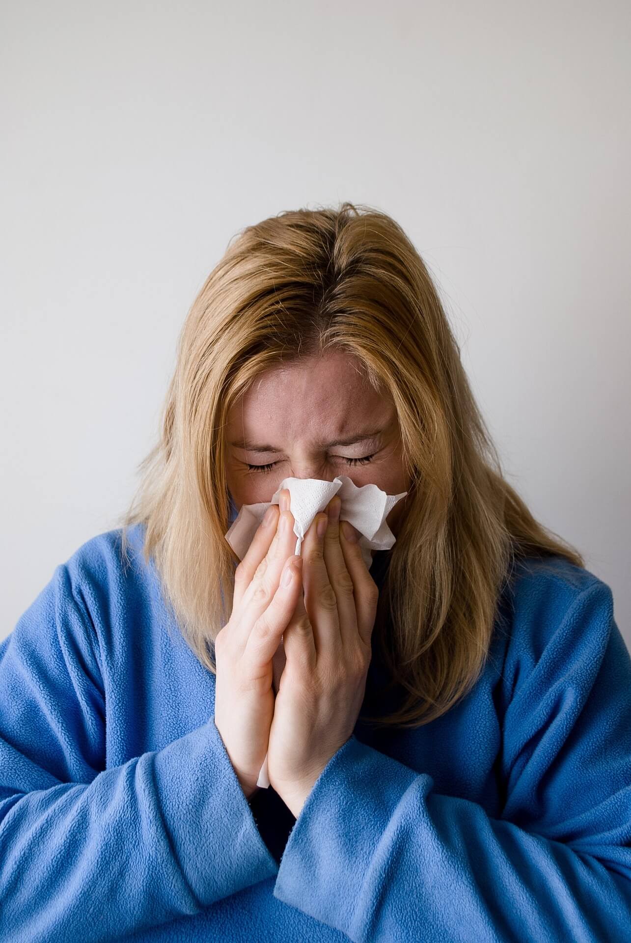 woman in blue dressing gown sneezing into a tissue