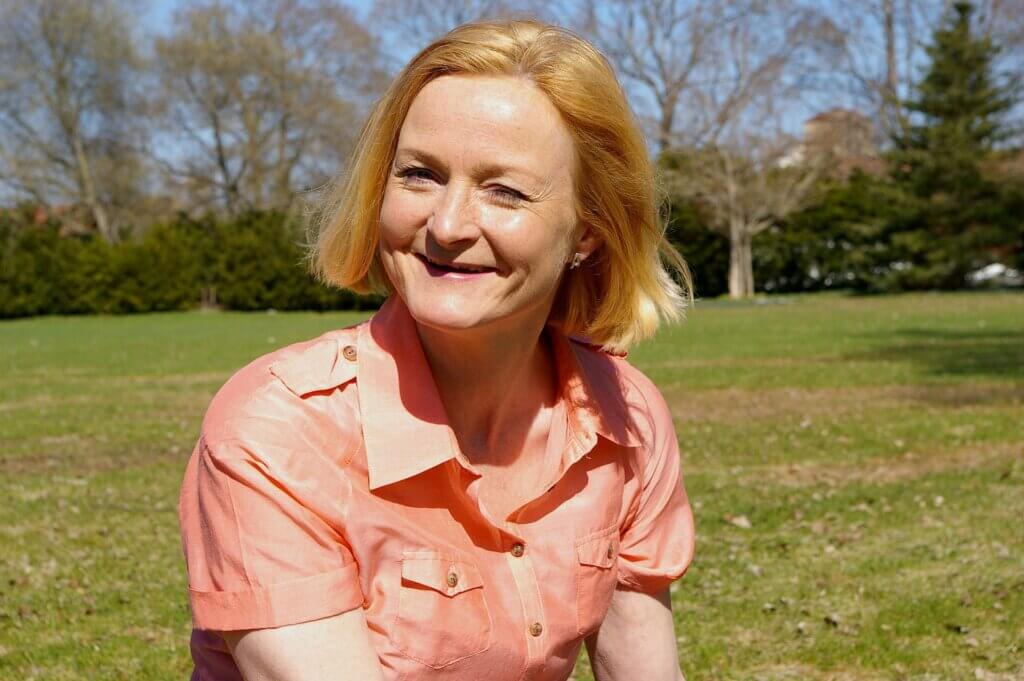 Woman smiling at the camera sitting outside in front of some trees