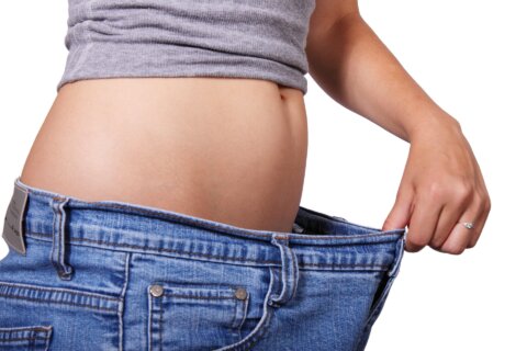 Picture of a woman showing her belly and holding out jeans that are too big to demonstrate her weight loss.