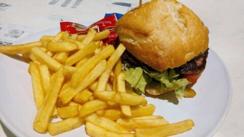 A hamburger with lettuce, chips and a packet of ketchup on a plate