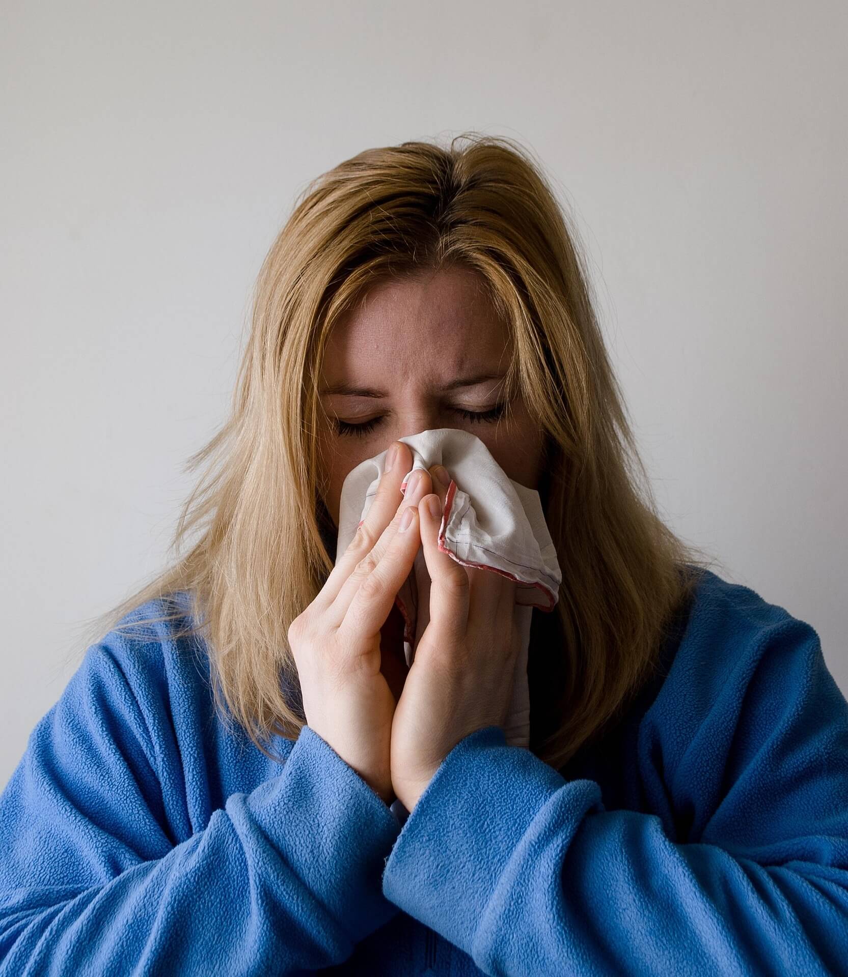 Woman wearing a dressing gown with messy hair sneezing into a paper tissue