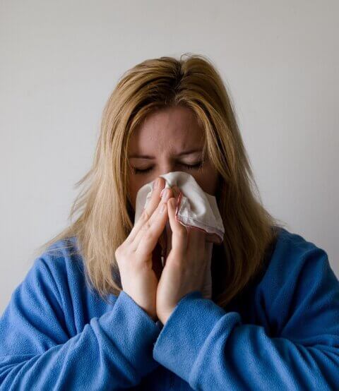 Woman with tousled hair in a blue dressing gown sneezing into a tissue.