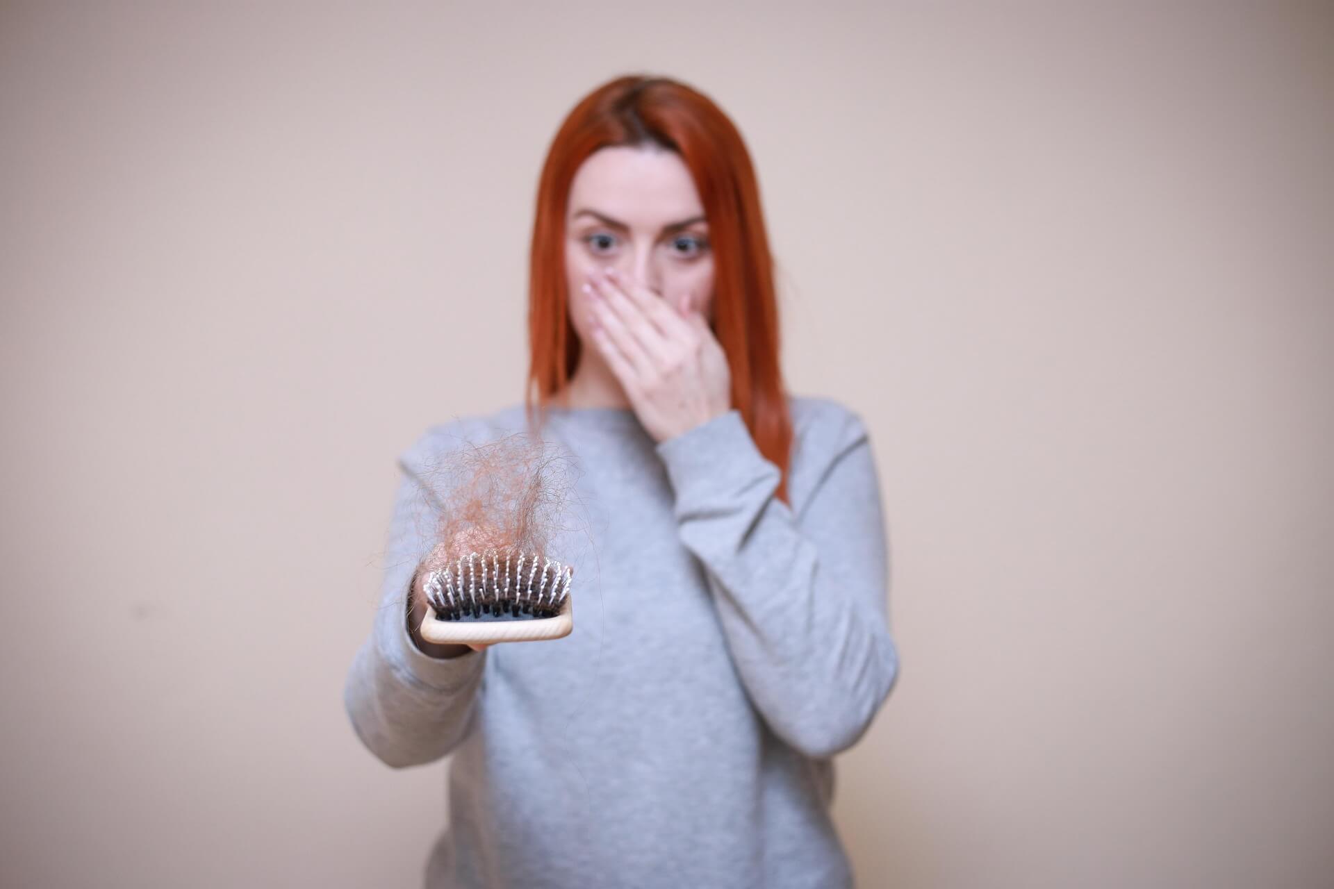 Woman examining hair loss in a hairbrush, a side effect some experience with weight loss injections