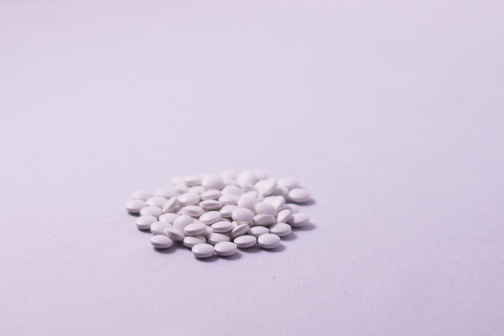 A small pile of white tablets on a pale pink surface. Morning-after pills